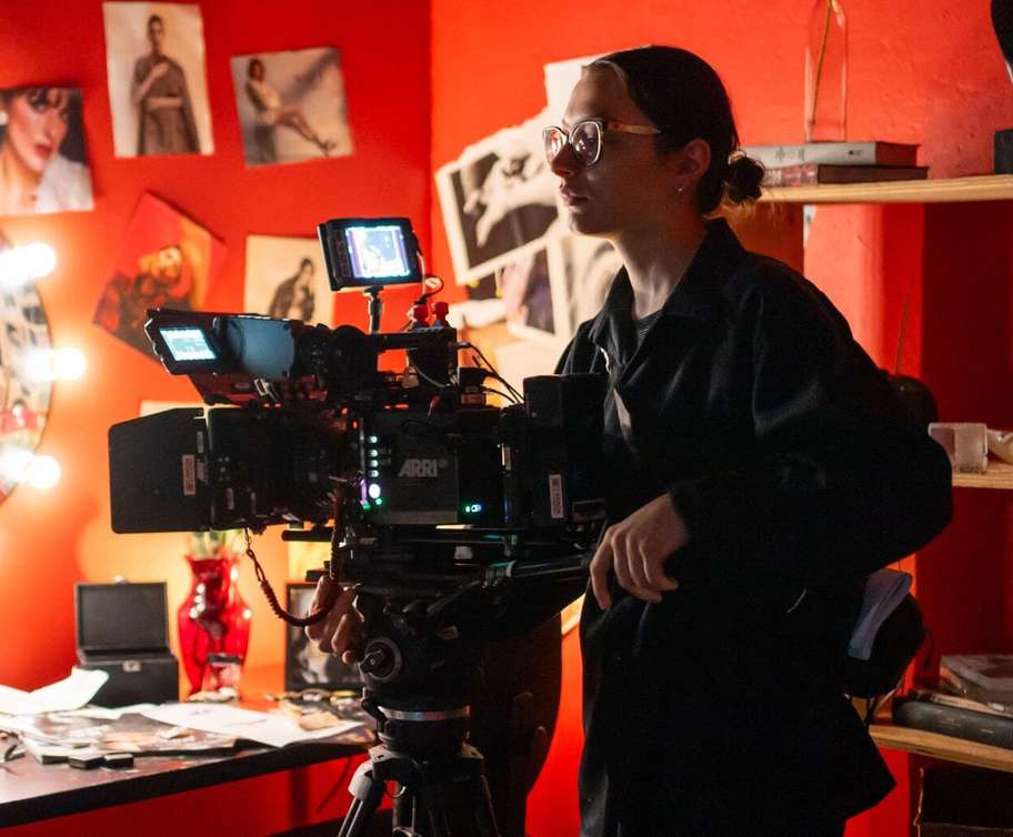 High school student filmmaker operating a professional ARRI cinema camera for a virtual presentation in a red studio.